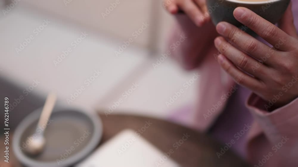 An unrecognizable woman takes a relaxing coffee break, enjoying her cappuccino while working remotely on her laptop. An unrecognizable woman takes a relaxing coffee break, enjoying her cappuccino while working remotely on her laptop.