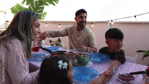 amily Gathering Around the Table for Outdoor Meal - A smiling family engages in conversation over a meal on a rooftop terrace. photo