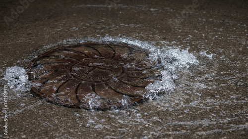 Water pipe burst, water Water flows out of the manhole onto the asphalt. The accident in the sewer. Leaking water supply system in the city on the road