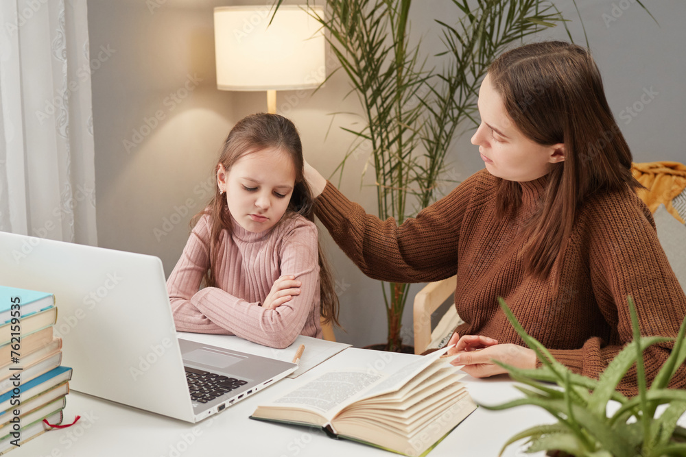 Online schooling for children. Homeschooling with computer resources. Mother's support in child's learning. Caucasian adult woman and daughter using laptop in home interior Online schooling for children. Homeschooling with computer resources. Mother's support in child's learning. Caucasian adult woman and daughter using laptop in home interior