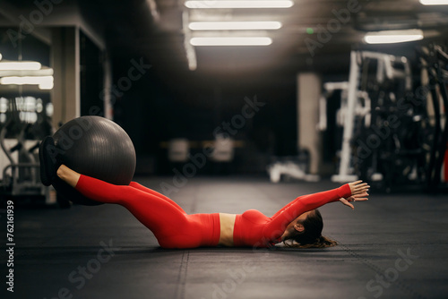 A sportswoman in shape is doing exercises for abs with pilates ball at gym.
