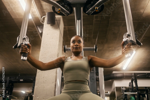 Front view of a black sportswoman doing exercises for chest on pec deck machine. photo