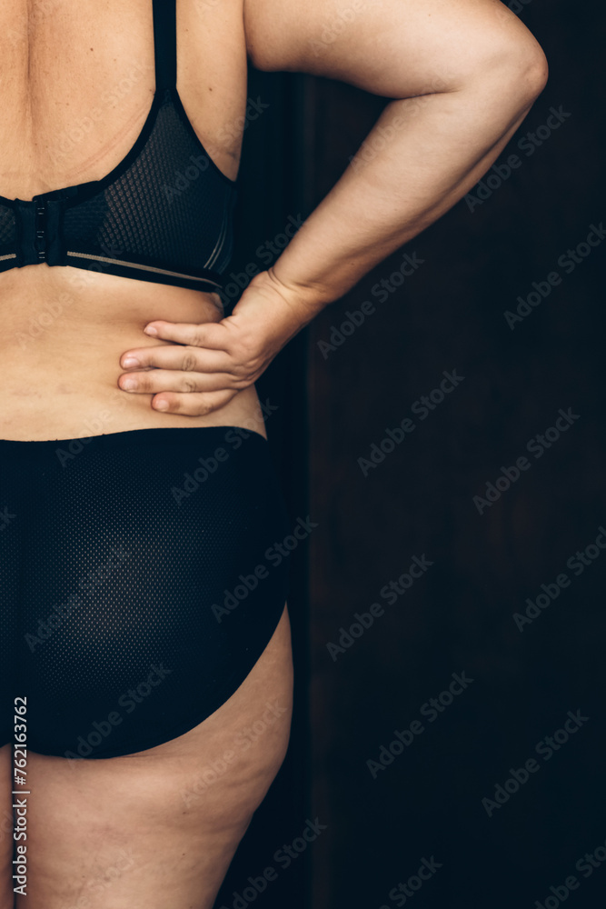 Fototapeta premium Woman with back pain in black underwear. Capturing a moment of discomfort, a woman clasps her lower back.