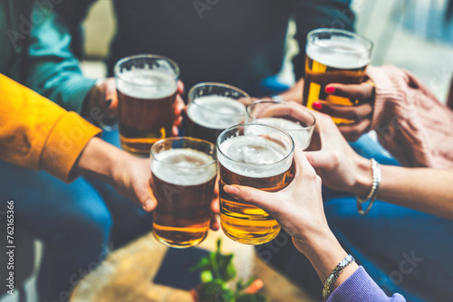 Group of people drinking beer at brewery pub restaurant - Happy friends enjoying happy hour sitting at bar table - Closeup image of brew glasses - Food and beverage lifestyle concept photo