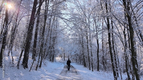 Man walking through winter snowy forest on country road, aerial follow view