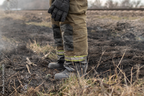 Firefighter extinguishes dry grass. Firefighter inspects place of ignition.