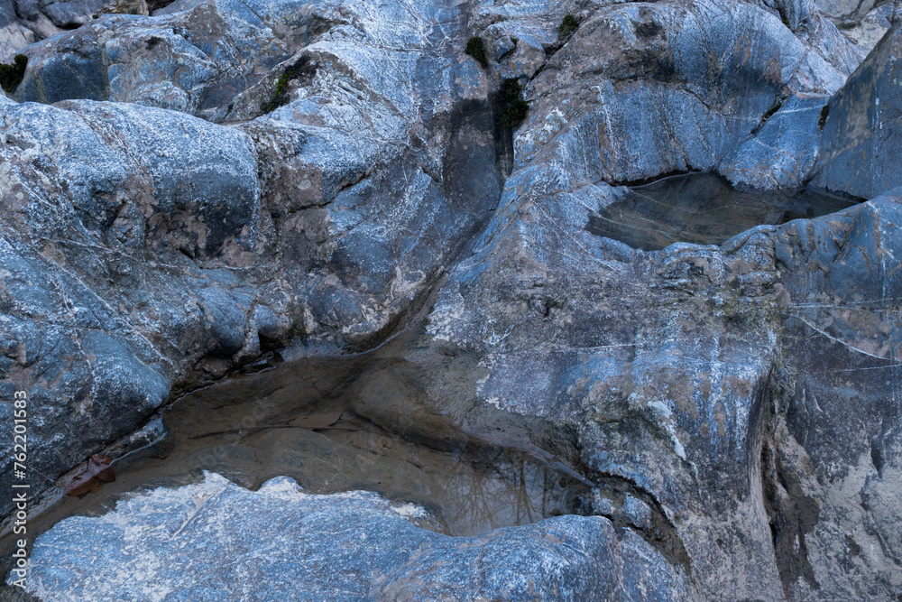 Naklejka premium Small puddle in blue rock close up, dent in stone filled with water during blue hour