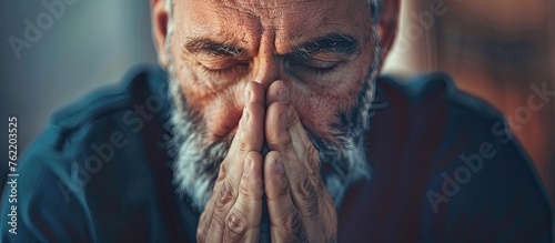 An older man with a disfigured jaw gestures with his wrinkled hands, covering his face. His electric blue eyes show a mix of worry and happiness in this photo caption art photo
