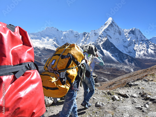 The adult sherpa porters carrying heavy backpacks and sacks in the Himalayas at Nepal, in the background the mountain of Ama Dablam photo