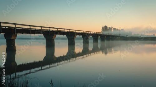 The soft hues of dawn cast a peaceful glow over a wooden bridge reflecting on a still river in the countryside.