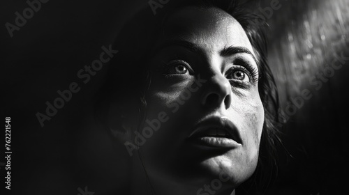 A dark room with a single spotlight on a woman's face, conveying a sense of exposure and vulnerability.
