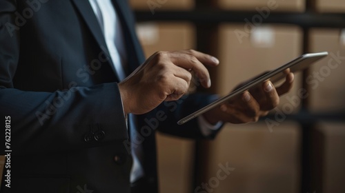 Focused executive navigating a digital tablet amidst storage shelves in a warehouse.