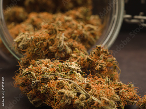 Dry and trimmed cannabis buds out of a glass jar on a gray background