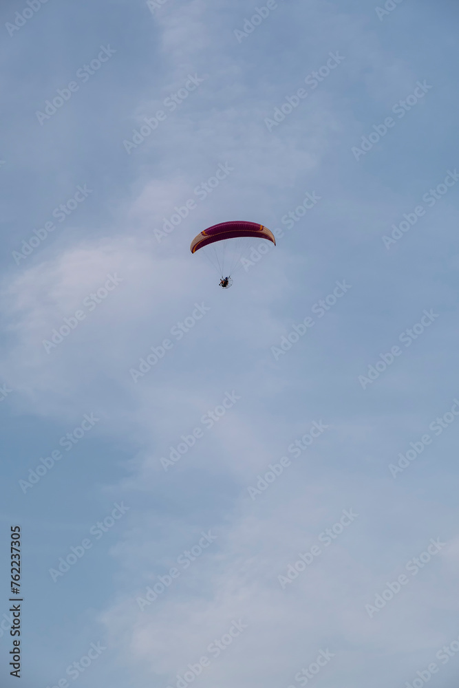 A paraglider or paramotor flying over a beautiful blue sky with white clouds over the beach.Real Photo A paraglider or paramotor flying over a beautiful blue sky with white clouds over the beach.Real Photo