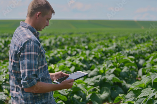 A thoughtful a male farmer standing and using tablet to monitor crop growth in a field. 