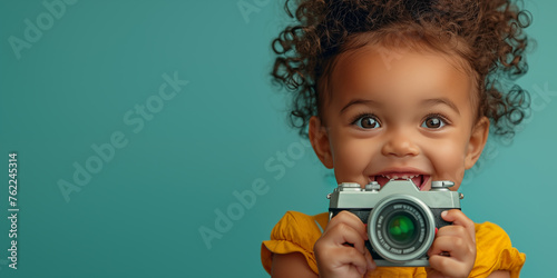 Cute, little baby holding camera over teal background. Banner with copyspace. Shallow depth of field.