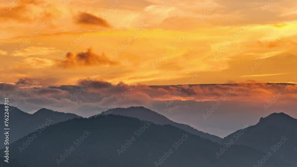 Golden sky with fast moving clouds over spring mountains at sunrise time lapse