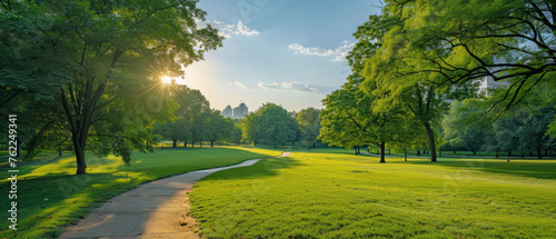 A serene park scene with a winding pathway amidst lush green grass, illuminated by the warm glow of the rising sun peeking through the leaves of mature trees.