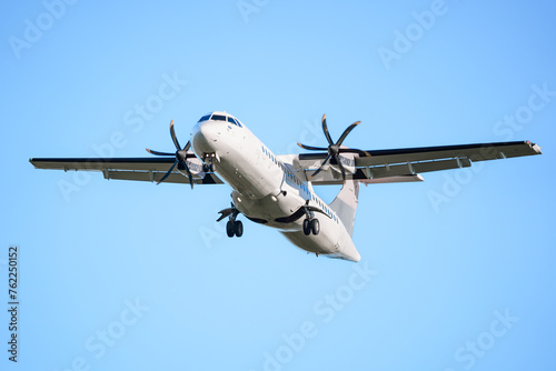 ATR 72 airplane, a twin-engine turboprop short-haul regional passenger aircraft. Landing airplane. Blue background. Clear sky.