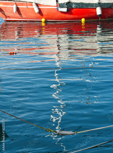 Red boat and boat water reflexion in water. Abstract distorted red boat elements in water. Blue water surface. Ripples reflex element in the lake Garda. Mirroring wave background. Abstract texture.