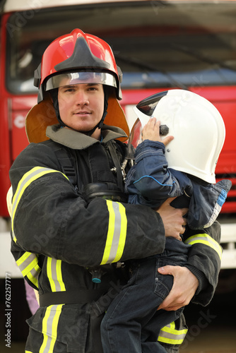 fireman wearing Fire Fighter turnouts and red helmet, holds child in his arms