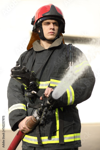 half-height portrait of fireman holds and adjust nozzle and fire hose spraying high pressure water