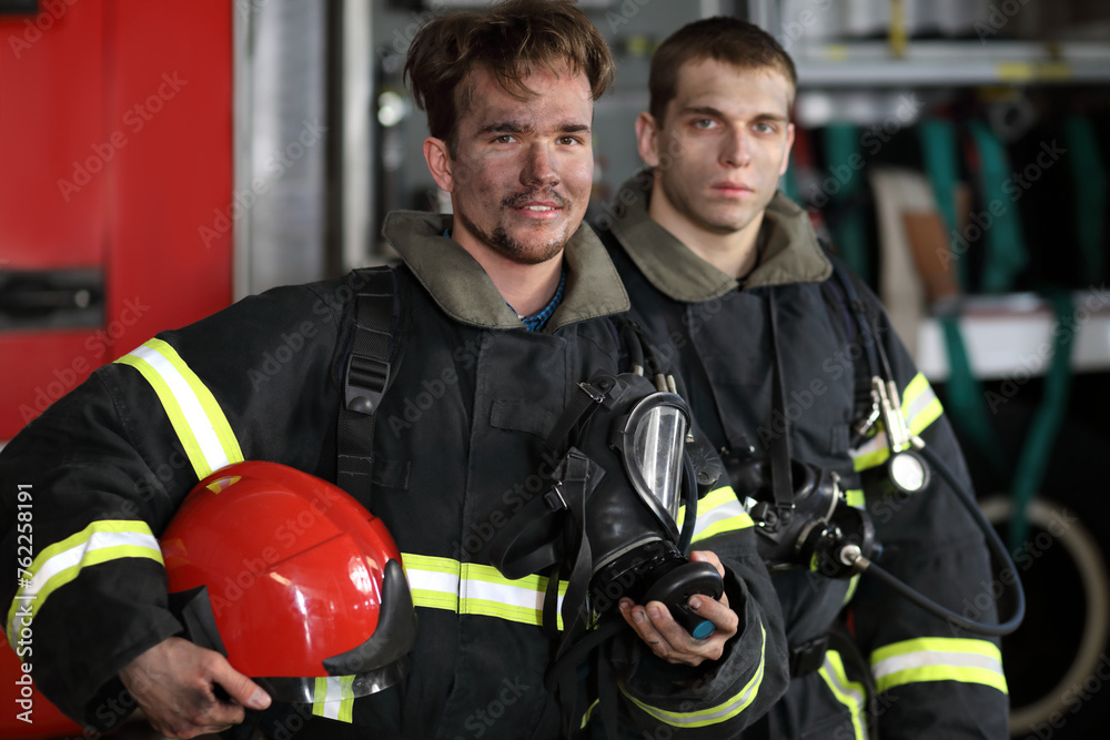 Two firefighters in protective suits standing against fire engine Two firefighters in protective suits standing against fire engine