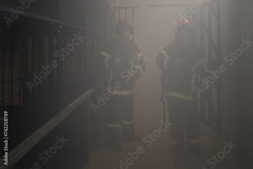 Two firemen in smoky environment hold protective masks in smoke chamber