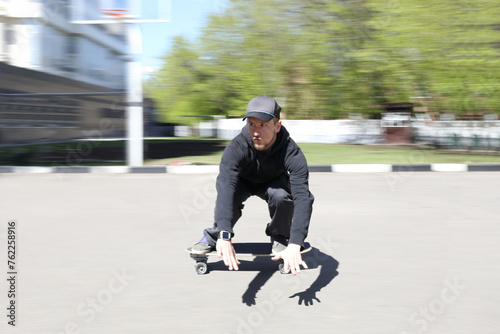 cool young skateboarder in black clothes, baseball cap riding skateboard