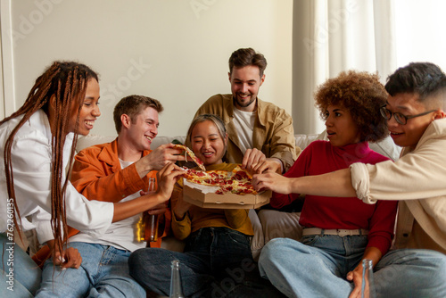 multiracial group of young people at house party eating pizza and drinking beer and having fun with friends