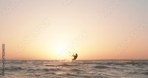 Silhouette of a kite surfer riding a kite surf at sunset. Kitesurfing. Watersport summer adrenaline activity