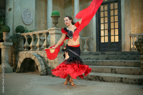 Beautiful woman in costume Carmen dancing with fan in an old middle hall