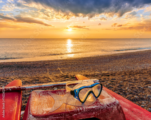 beautiful cloudy morning landscape with diving mask on a red old boat on foreground, sand beach, blue sea with surf and waves and cloudy sunset or sunrise on background
