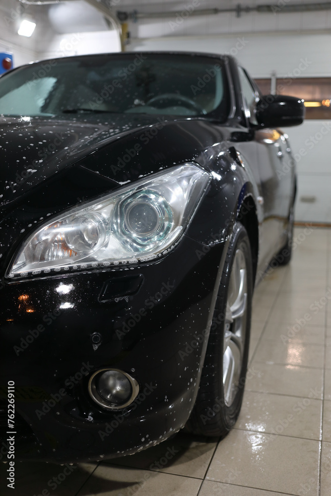 Front of black car with detergent drops during washing