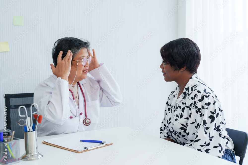 Obstetrician-gynecologist in dialogue with patient, hands to head in gesture of explanation, office setting denotes professional medical advice.Senior gynecologist listens actively to patient concerns Obstetrician-gynecologist in dialogue with patient, hands to head in gesture of explanation, office setting denotes professional medical advice.Senior gynecologist listens actively to patient concerns