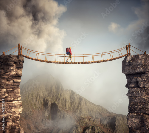 Hiker walking on a suspension bridge between mountains.