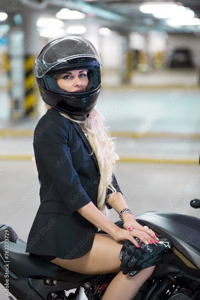 Young girl with long blond hair is sitting on the black bike at parking. Young girl with long blond hair is sitting on the black bike at parking.