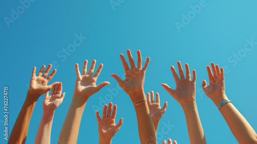 Energetic hands reaching up against a clear blue sky, reflecting hope and collective effort. Group of young people's hands raised, outdoors