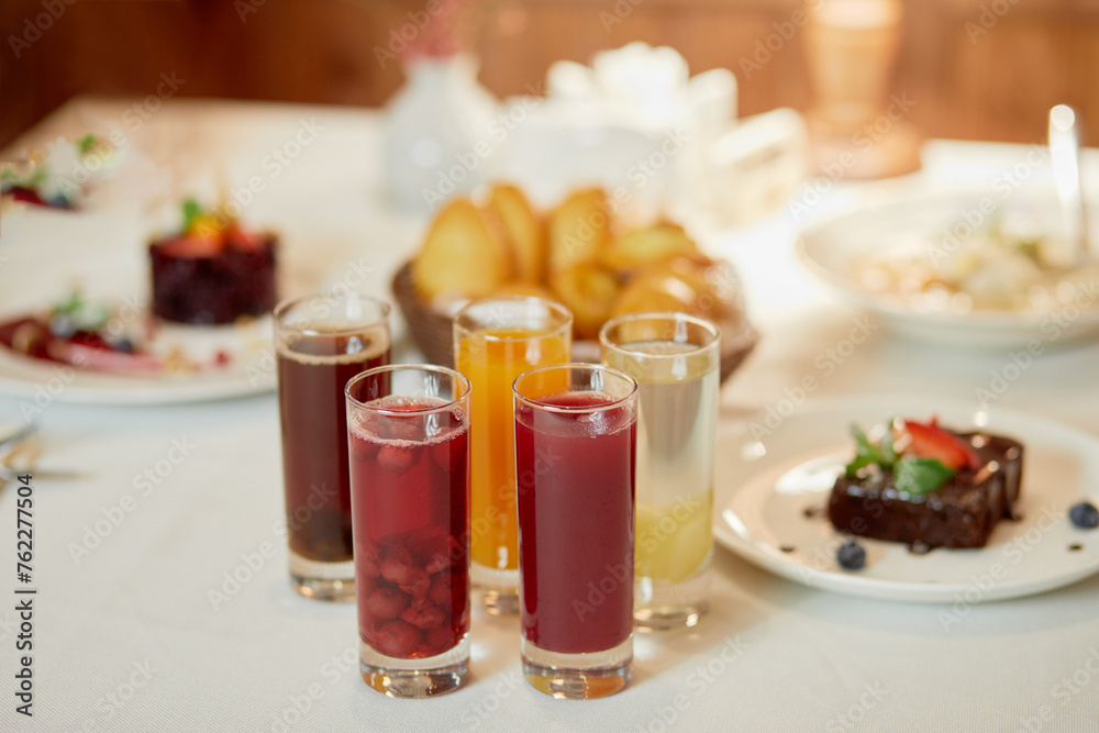 Several kinds of fruit beverages in glasses and cakes on table, shallow dof.