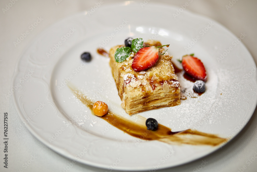 Layer cake with mint, strawberry, blueberry and sauce on plate.