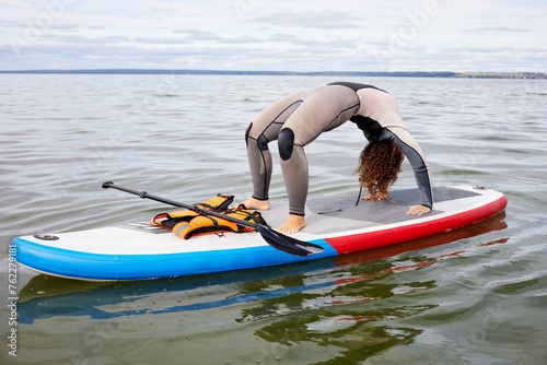 Woman in surfer suit stands in crab position on inflatable SUP board on water. © Pavel Losevsky