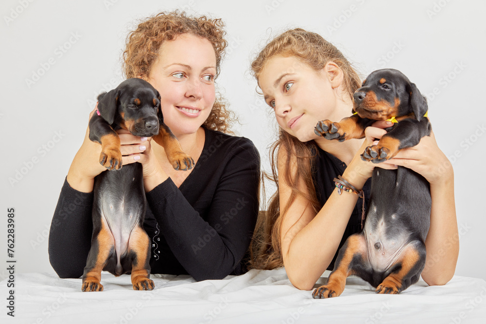 Mother and daughter hold little doberman puppies in their arms. Mother and daughter hold little doberman puppies in their arms.