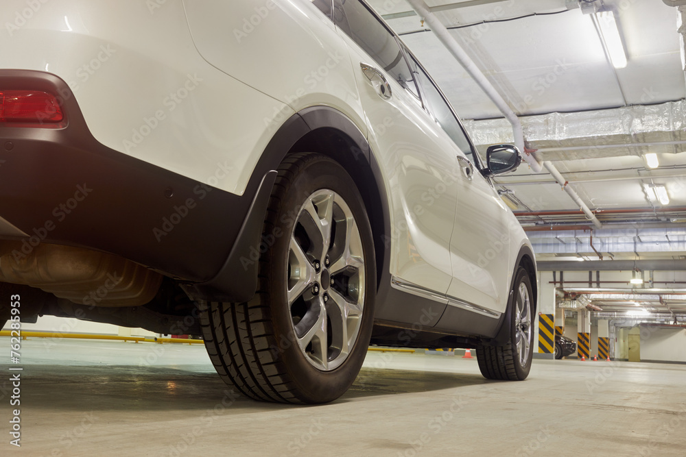 Sports white car at underground parking, low angle side rear view.