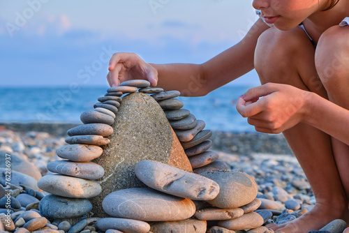 The child's hands lay pebbles, stones in a tower on the beach in summer, close-up.