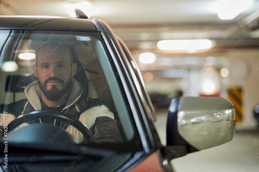 Bearded man sits on driver seat in car at underground parking. Bearded man sits on driver seat in car at underground parking.