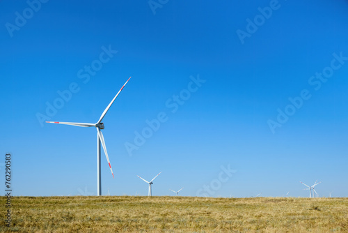 Wind turbines in the field against a blue sky in summer.