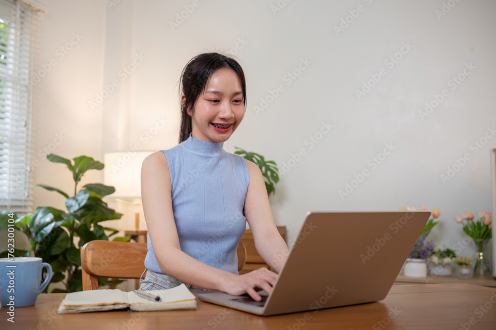 Young woman studying while sitting at the table with laptop computer and notebook at home Young woman studying while sitting at the table with laptop computer and notebook at home