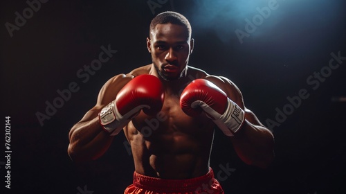Young muscular African American male boxer with red gloves on black background.