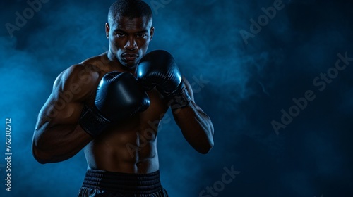 Young muscular African American man boxer with black gloves on, ready to fight. Dark blue background with smoke. © AiStock