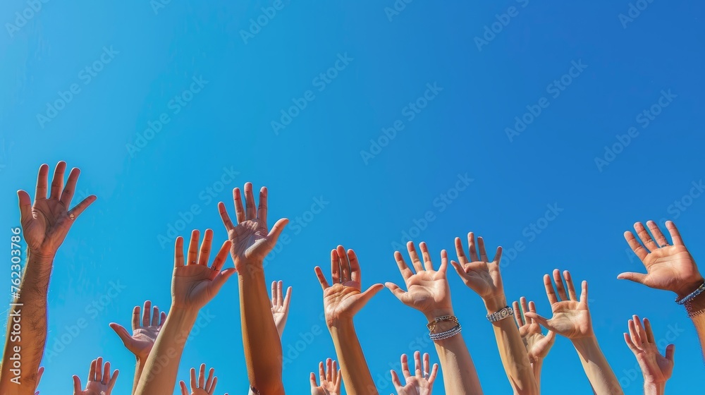 Energetic hands reaching up against a clear blue sky, reflecting hope and collective effort. Group of young people's hands raised, outdoors